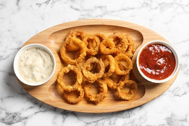 Photo of Homemade crunchy fried onion rings with sauces on marble table, top view
