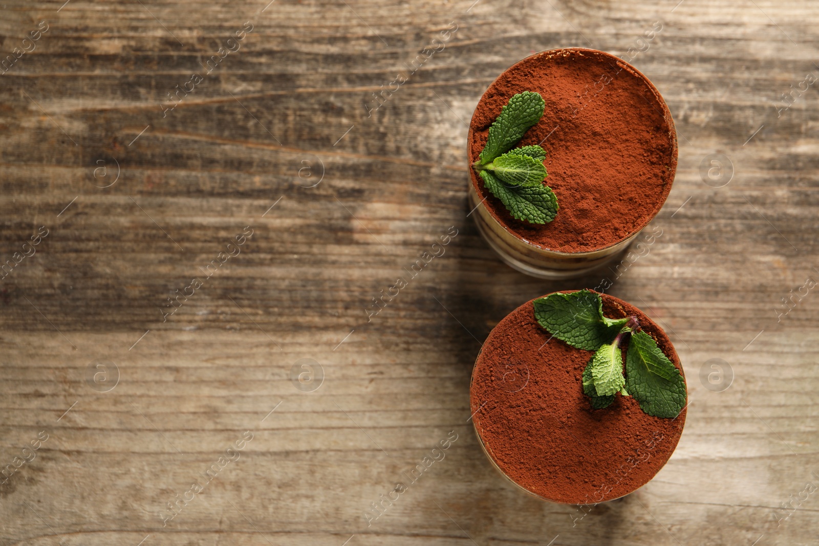 Photo of Tasty tiramisu and mint in glasses on wooden table, top view. Space for text