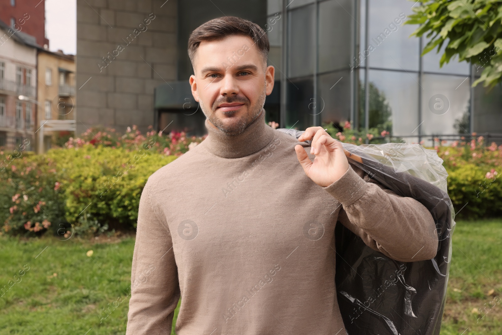 Photo of Man holding garment cover with clothes outdoors. Dry-cleaning service