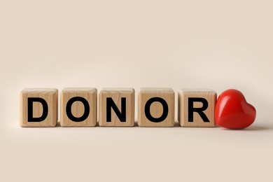 Photo of Wooden cubes with word Donor and small red heart on beige background