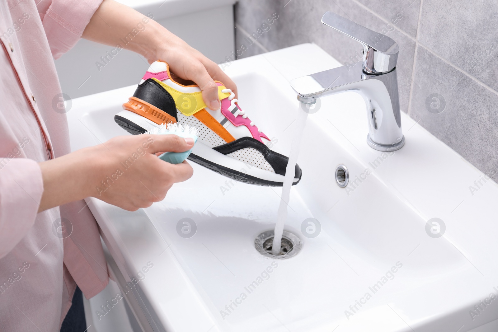 Photo of Woman washing stylish sneakers with brush in sink, closeup