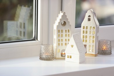 Beautiful house shaped candle holders on windowsill indoors, space for text