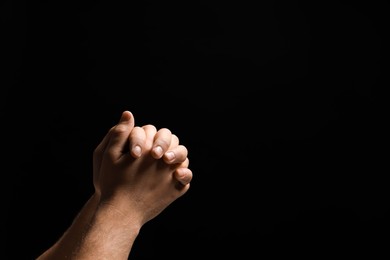 Photo of Religion. Christian man praying on black background, closeup. Space for text