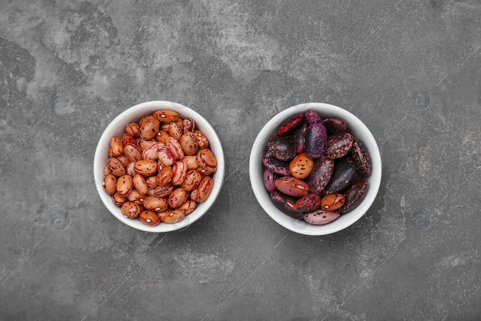 Photo of Bowls with different types of beans on grey table, flat lay