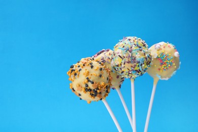 Photo of Delicious confectionery. Sweet cake pops decorated with sprinkles on blue background, closeup. Space for text