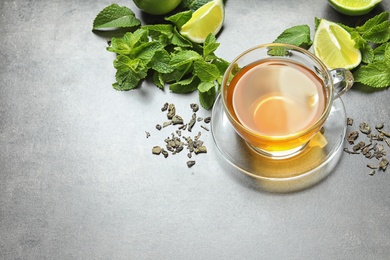 Photo of Cup with hot aromatic mint tea, lime, fresh and dry leaves on table
