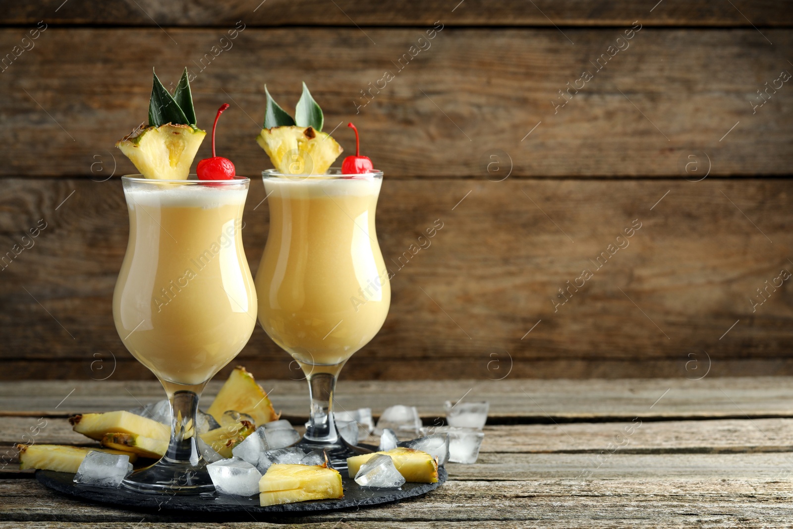 Photo of Tasty Pina Colada cocktails and ingredients on wooden table, space for text