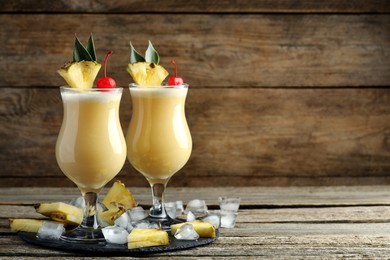 Tasty Pina Colada cocktails and ingredients on wooden table, space for text