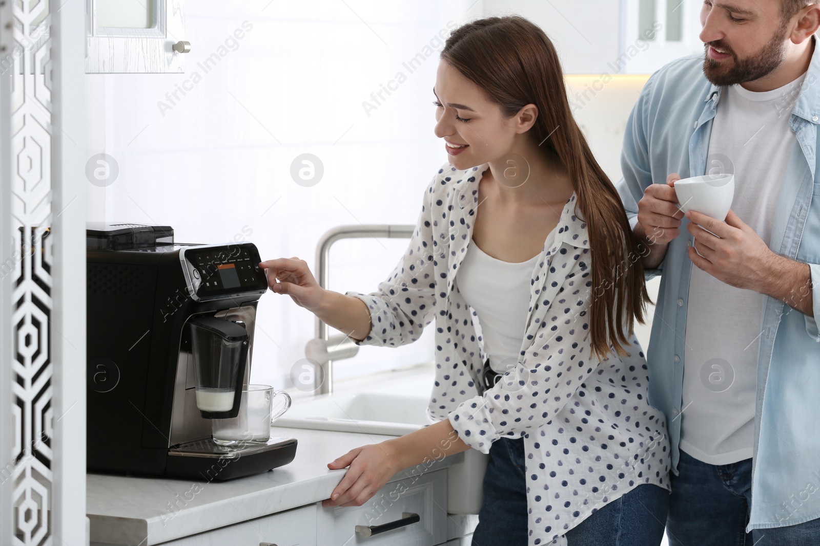 Photo of Happy couple preparing fresh aromatic coffee with modern machine in kitchen