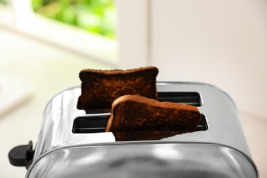 Modern toaster with slices of burnt bread against blurred background, closeup