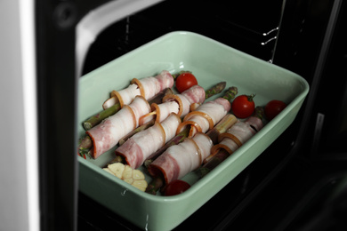 Photo of Uncooked bacon wrapped asparagus in baking dish on oven rack, closeup