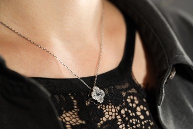 Photo of Woman wearing stylish metal chain with pendant, closeup. Luxury jewelry