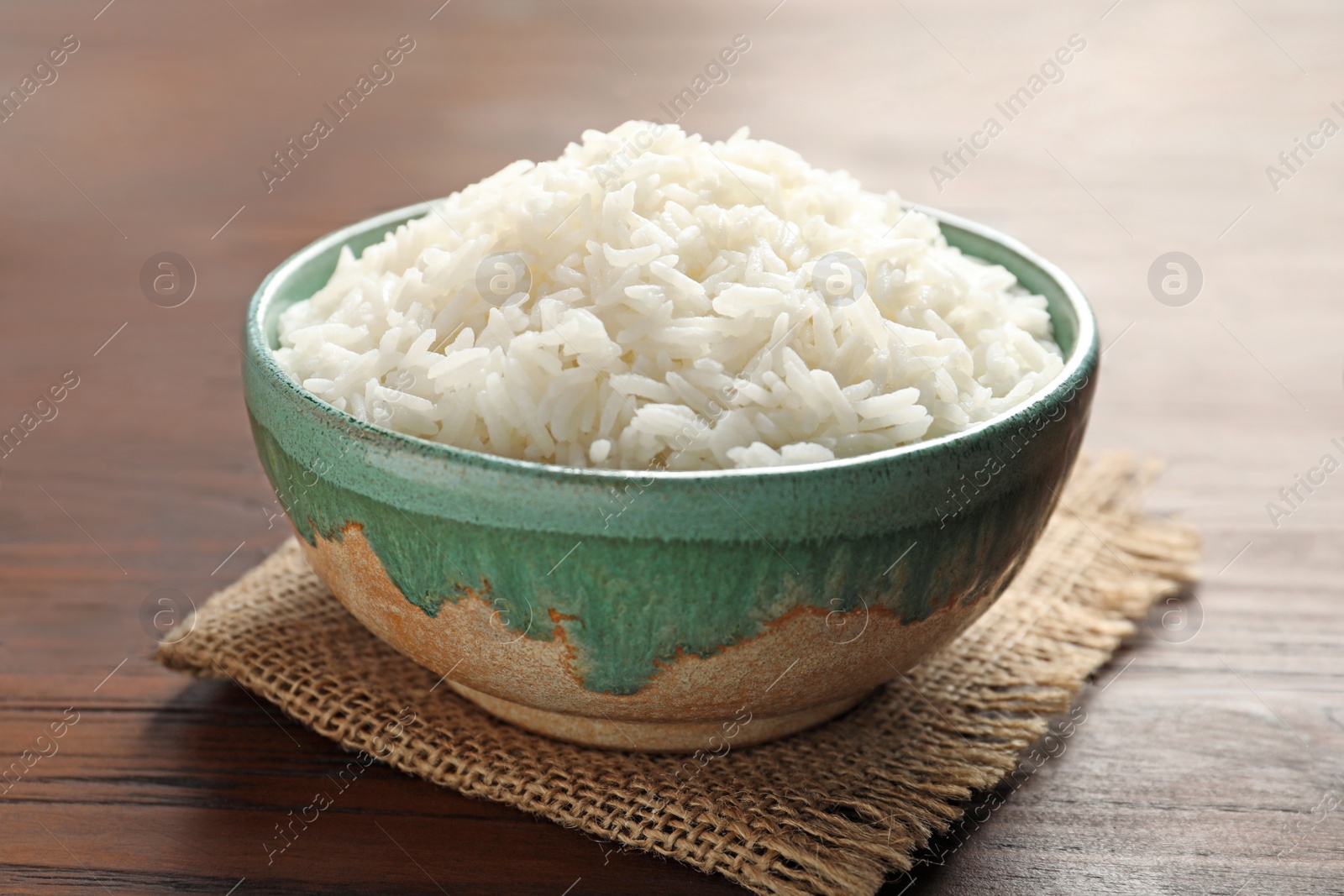 Photo of Bowl of tasty cooked white rice on wooden table, closeup