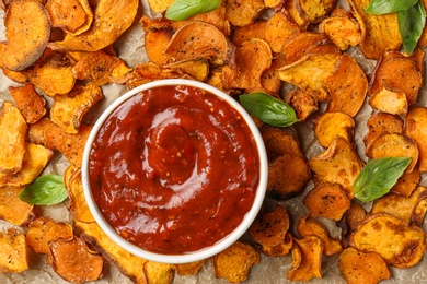Photo of Sweet potato chips and bowl of sauce on parchment, top view