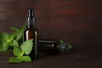 Photo of Glass bottles of nettle oil with leaves on wooden table. Space for text