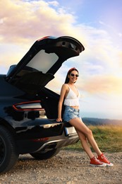 Photo of Happy woman sitting in trunk of modern car on roadside outdoors