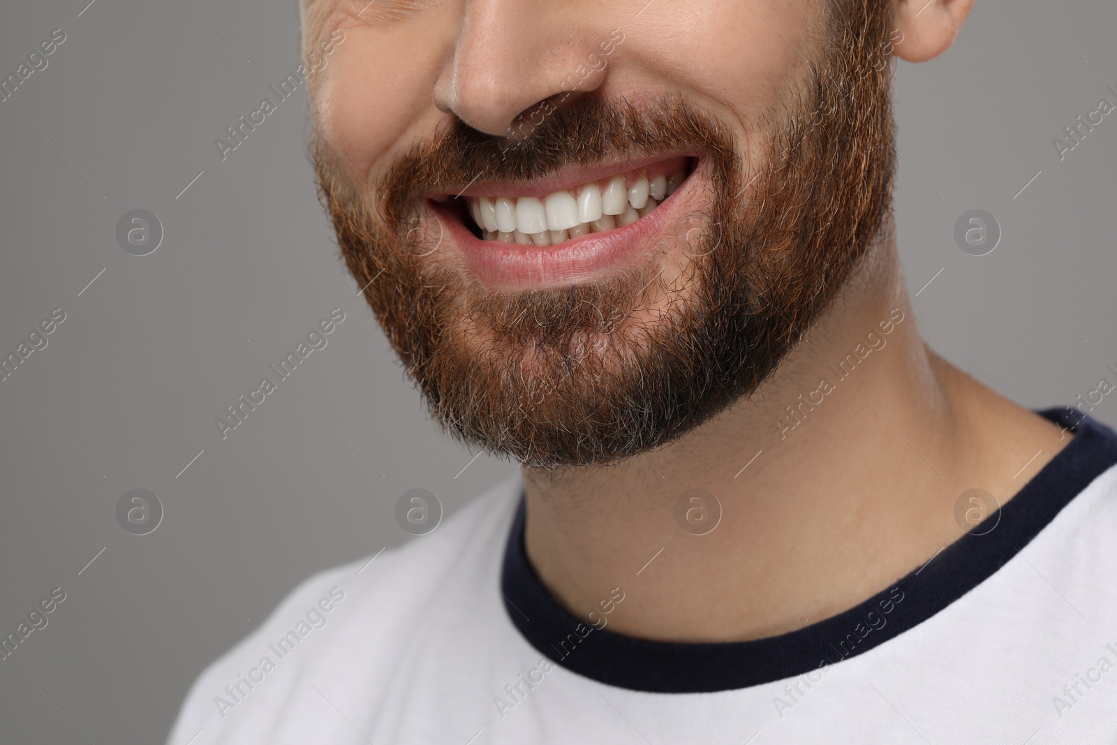 Photo of Smiling man with healthy clean teeth on grey background, closeup