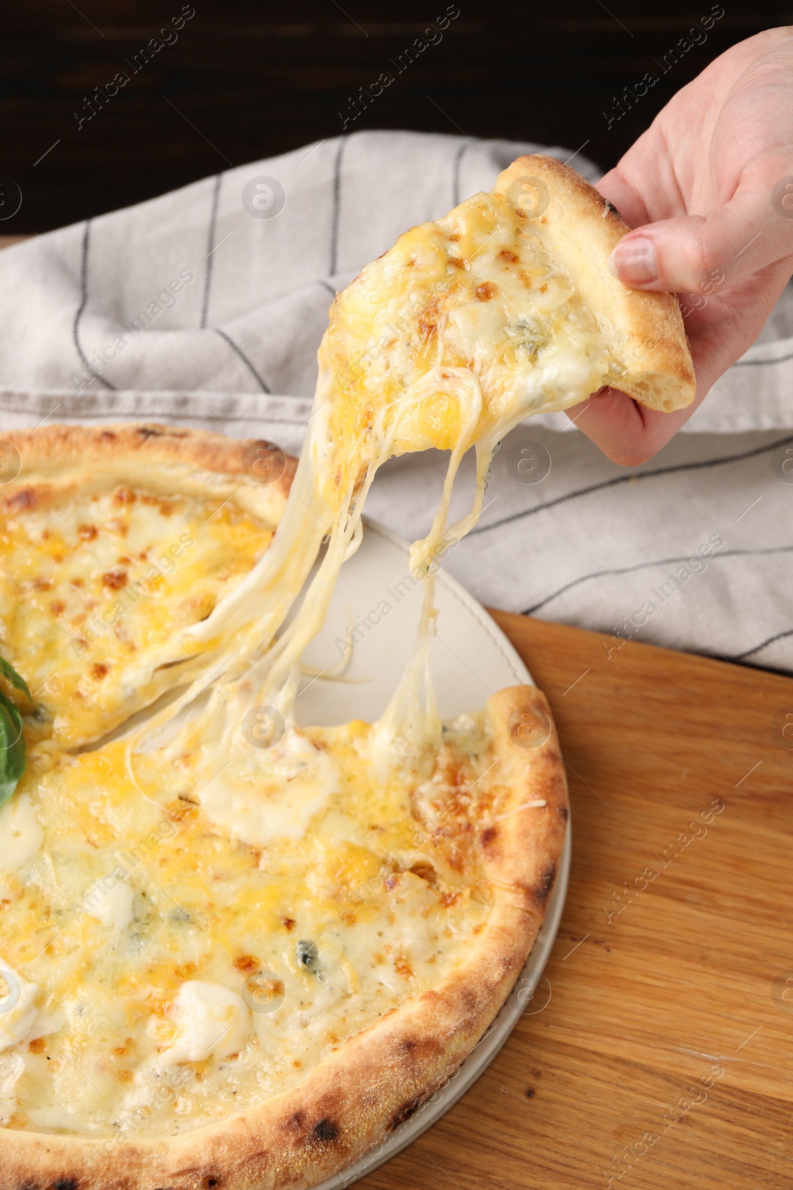 Photo of Woman taking piece of delicious cheese pizza at table, closeup