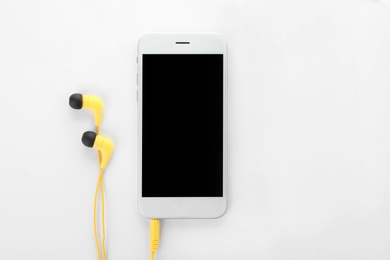 Photo of Smartphone with blank screen and headphones on white background, top view