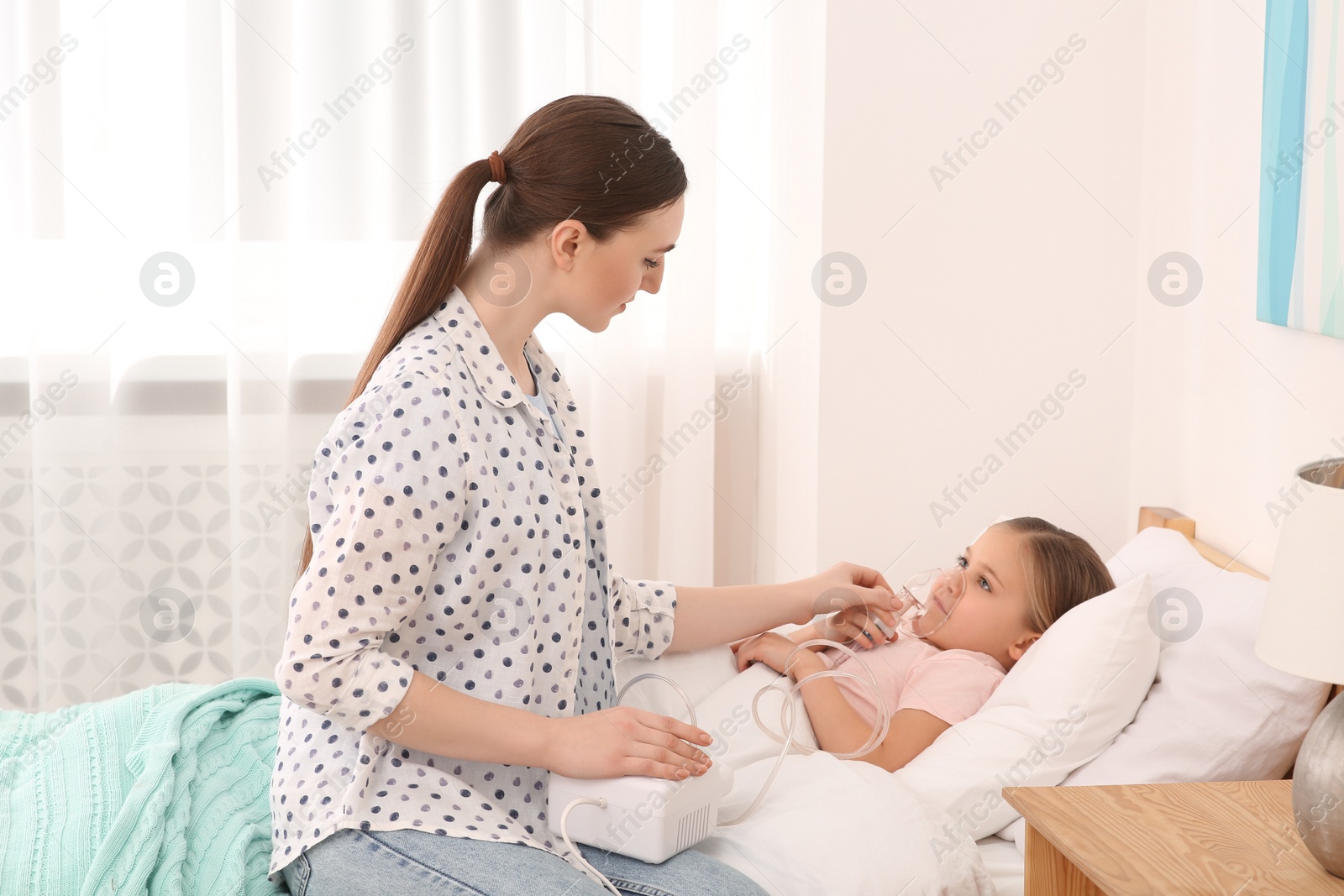 Photo of Mother helping her sick daughter with nebulizer inhalation in bedroom