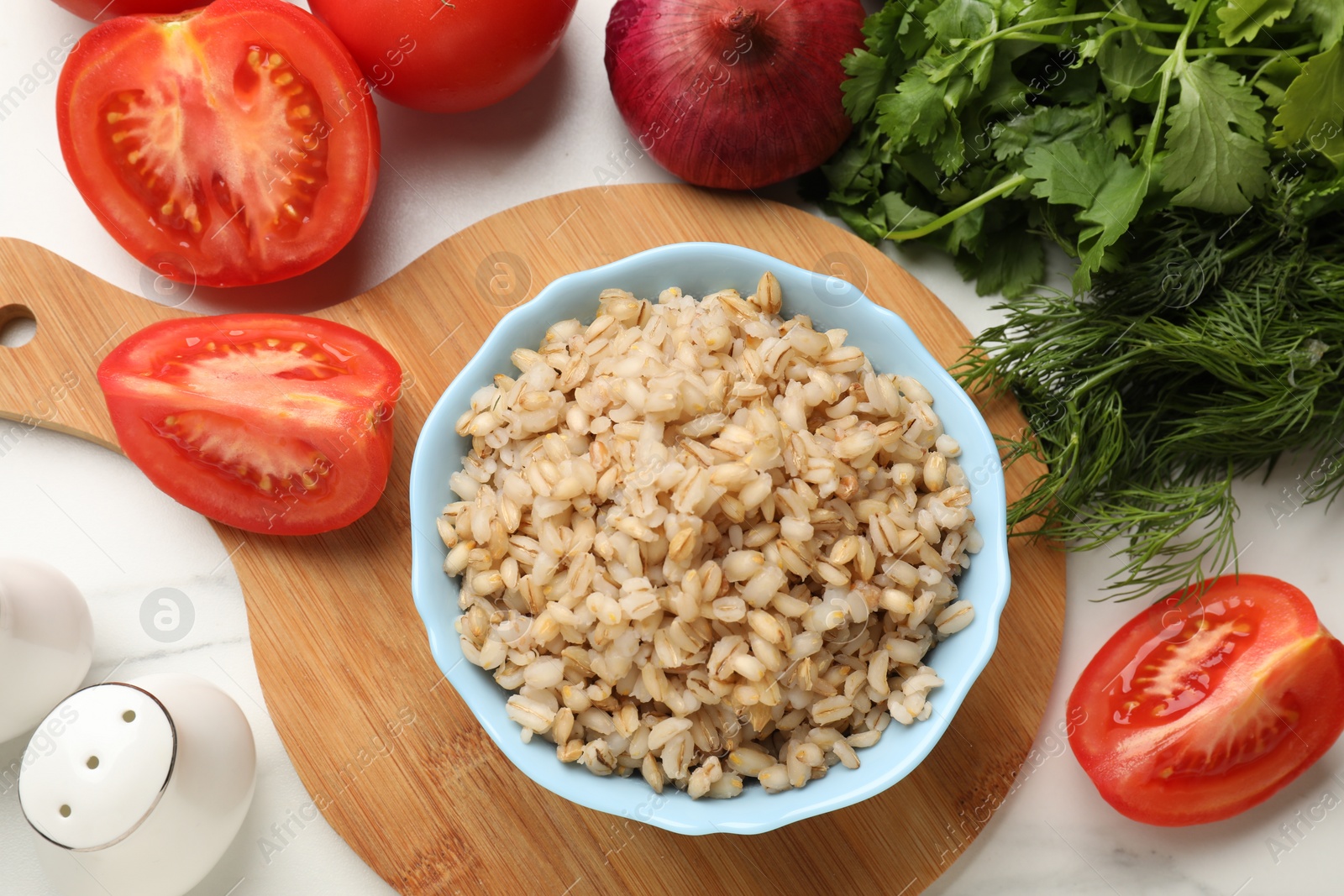 Photo of Delicious pearl barley in bowl served on white table, flat lay