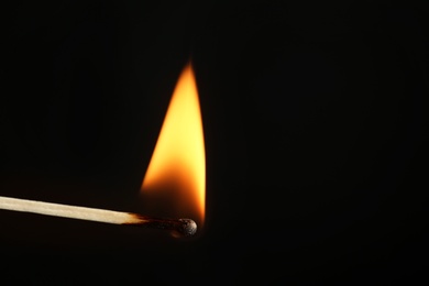 Photo of Burning matchstick on black background, closeup. Space for text