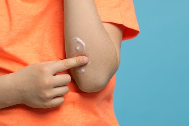 Photo of Child applying ointment onto elbow against light blue background, closeup. Space for text