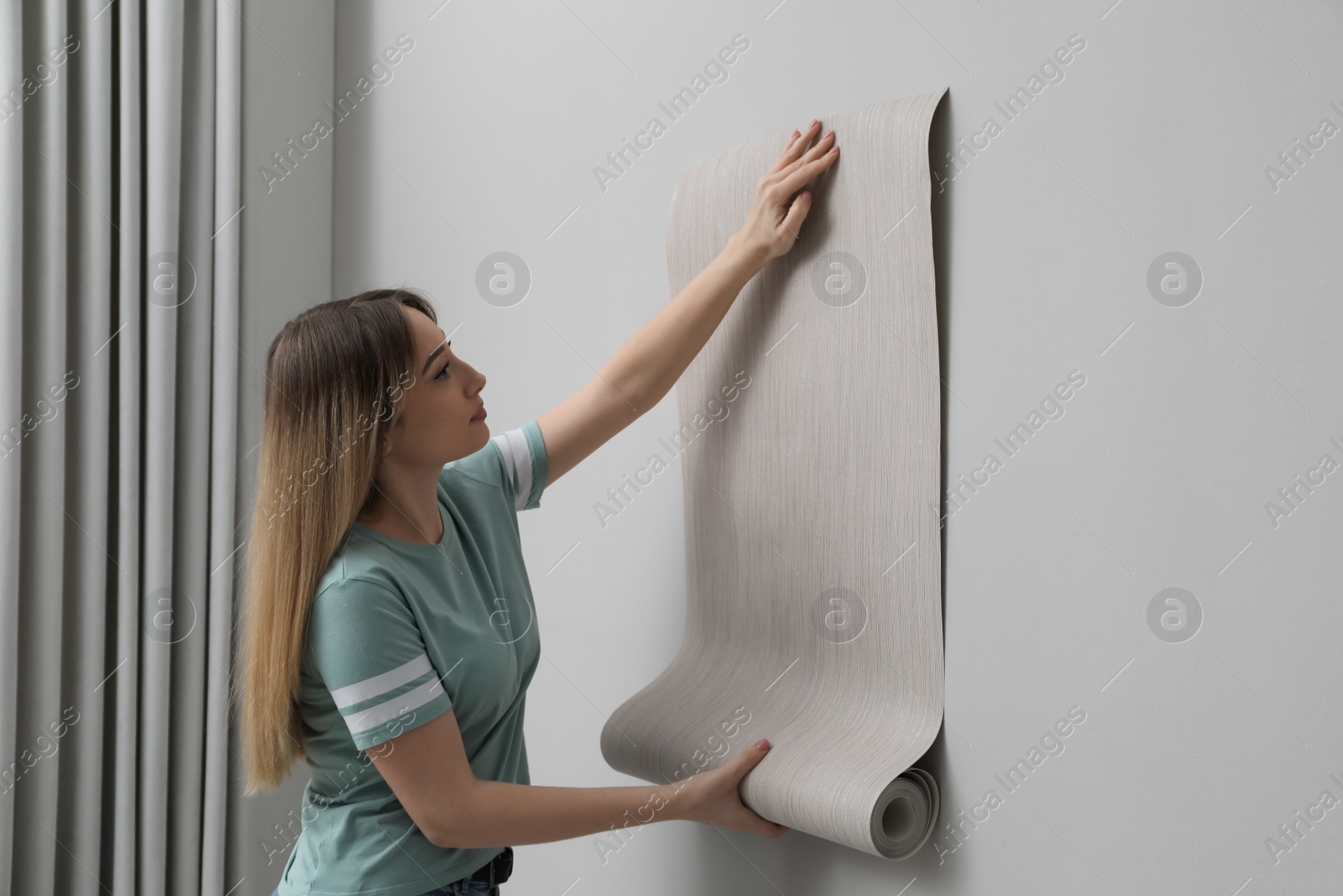 Photo of Woman hanging stylish wall paper sheet indoors