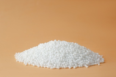 Pellets of ammonium nitrate on beige background, space for text. Mineral fertilizer