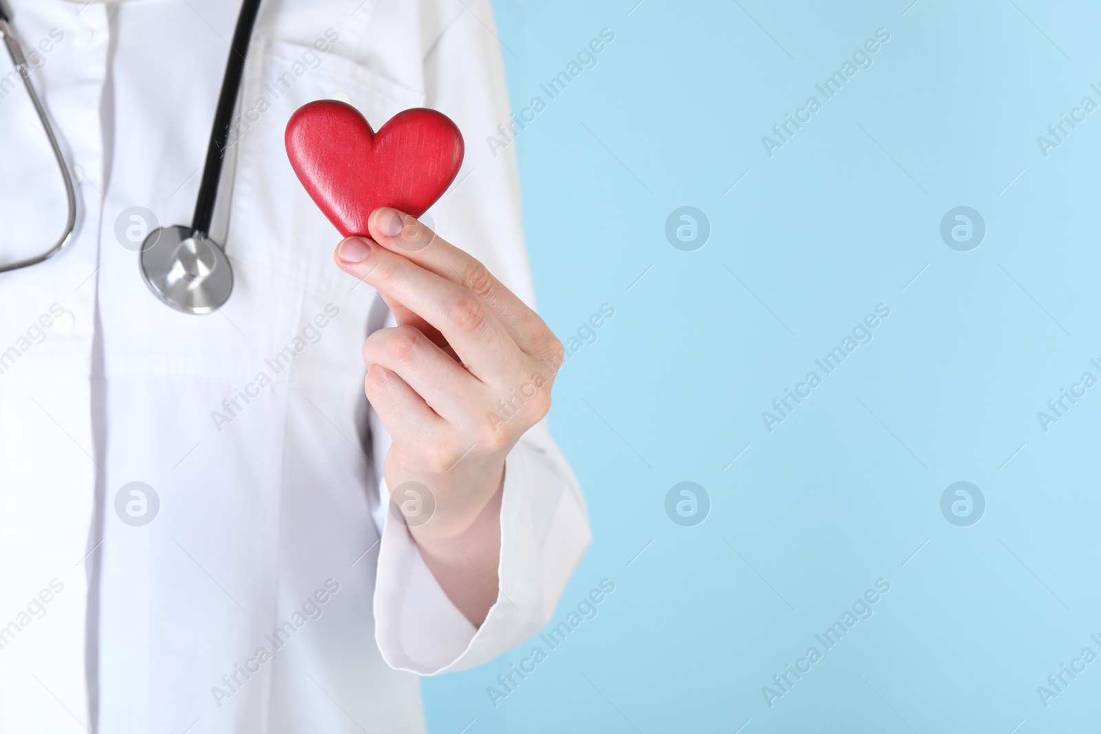 Photo of Doctor with red heart on light blue background, closeup. Space for text