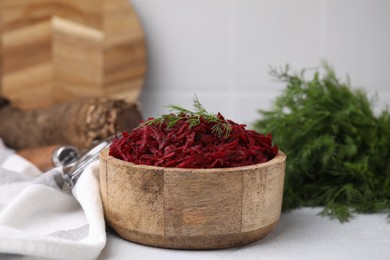 Grated red beet and dill in wooden bowl on table