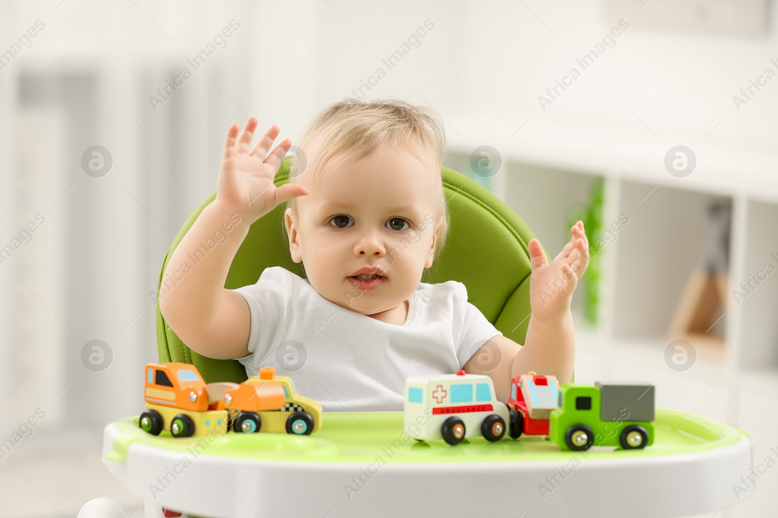 Photo of Children toys. Cute little boy playing with toy cars in high chair at home