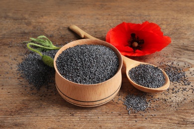 Wooden bowl of poppy seeds, spoon and flower on table