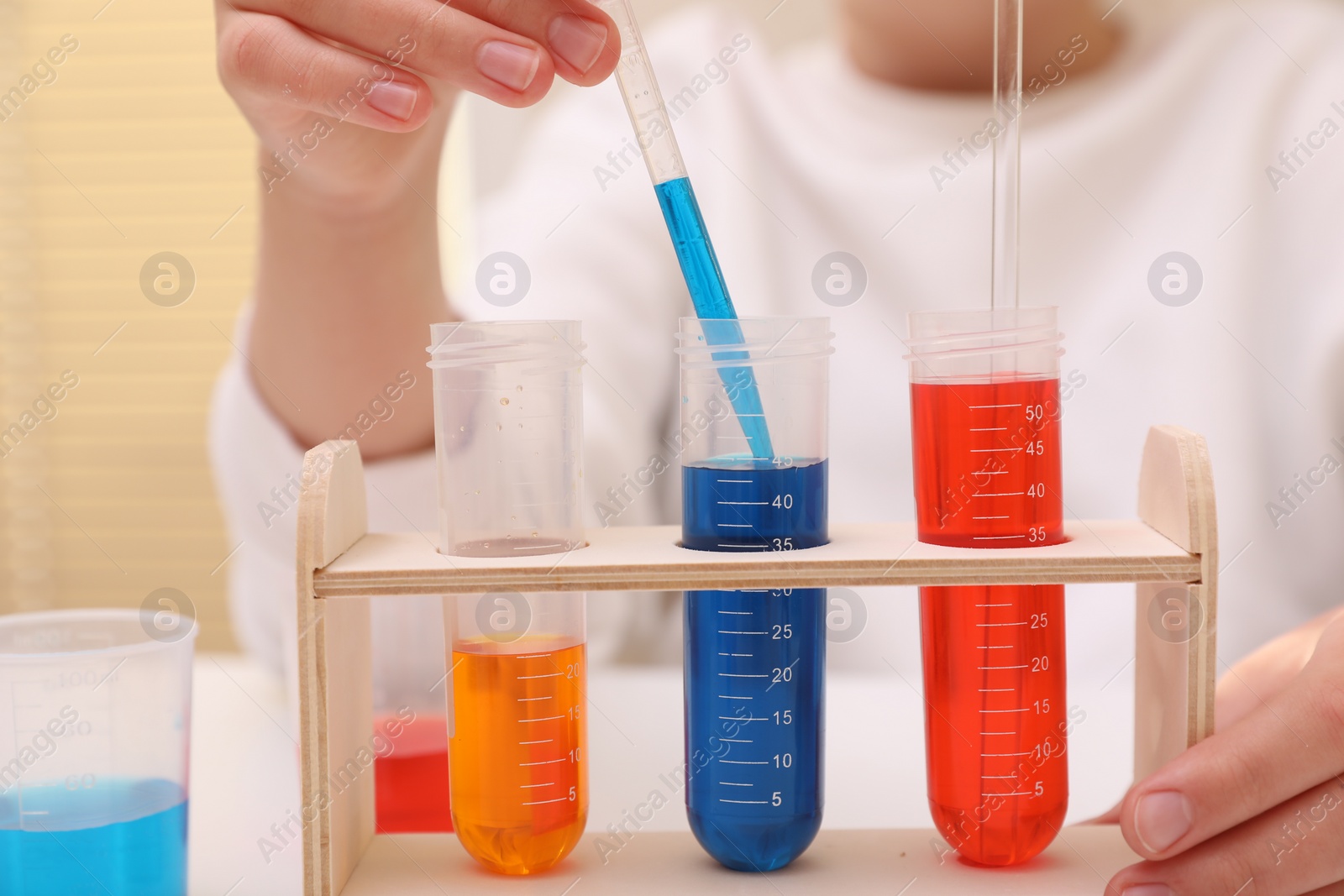 Photo of Girl mixing colorful liquids at white table indoors, closeup. Chemical experiment set for kids