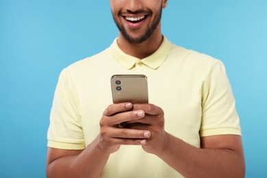 Man sending message via smartphone on light blue background, closeup