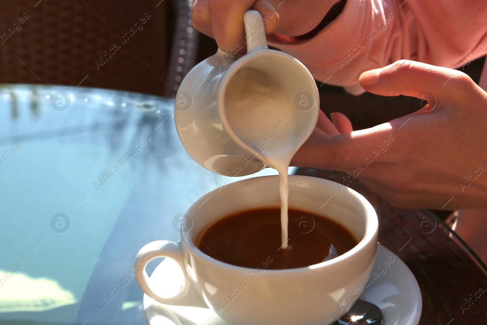 Photo of Woman pouring milk in coffee at table in cafe