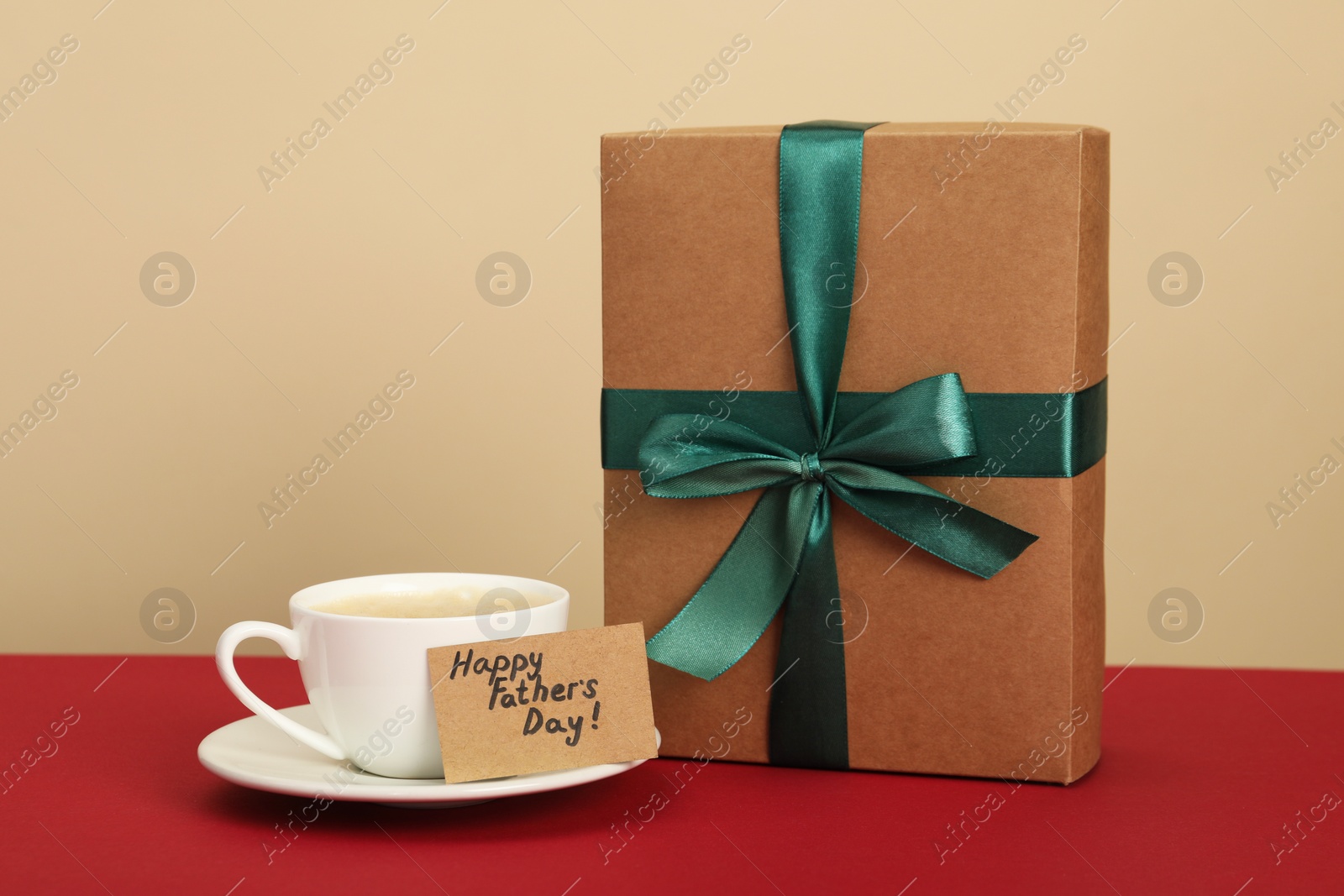 Photo of Happy Father's Day. Coffee cup, card with greetings and gift box on red table