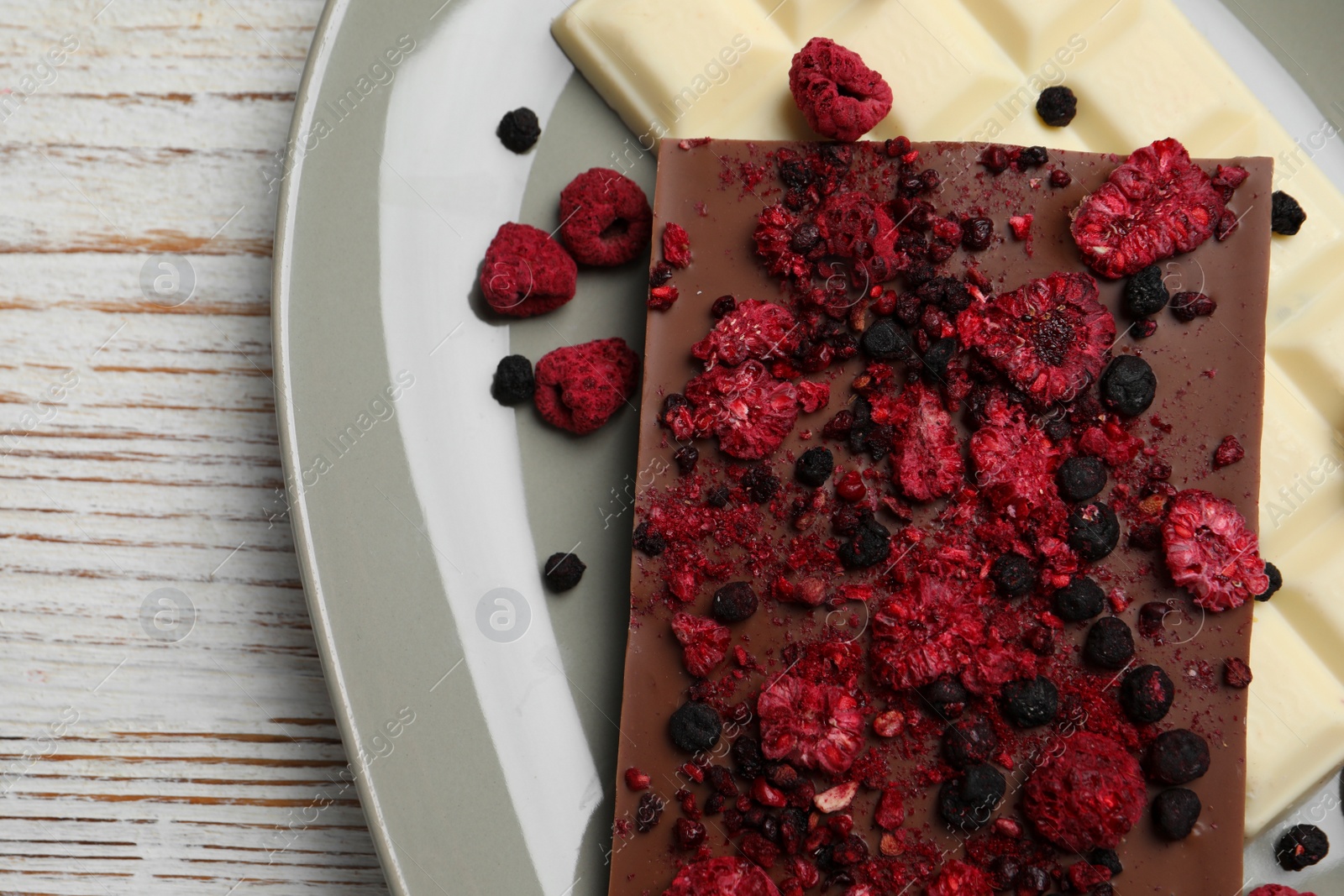 Photo of Plate and different chocolate bars with freeze dried fruits on white wooden table, top view