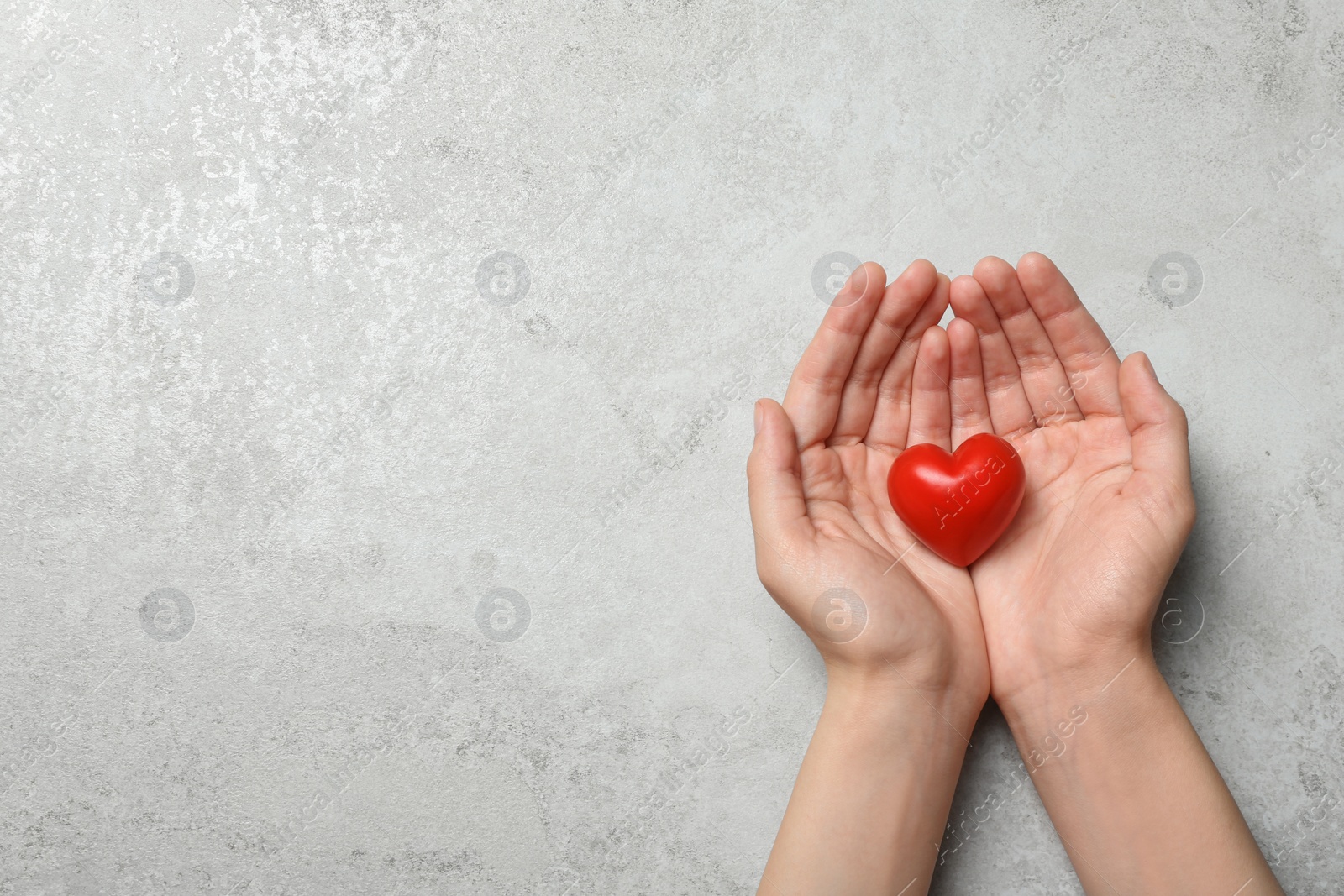 Photo of Woman holding heart on grey stone background, top view with space for text. Donation concept