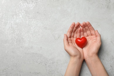 Woman holding heart on grey stone background, top view with space for text. Donation concept