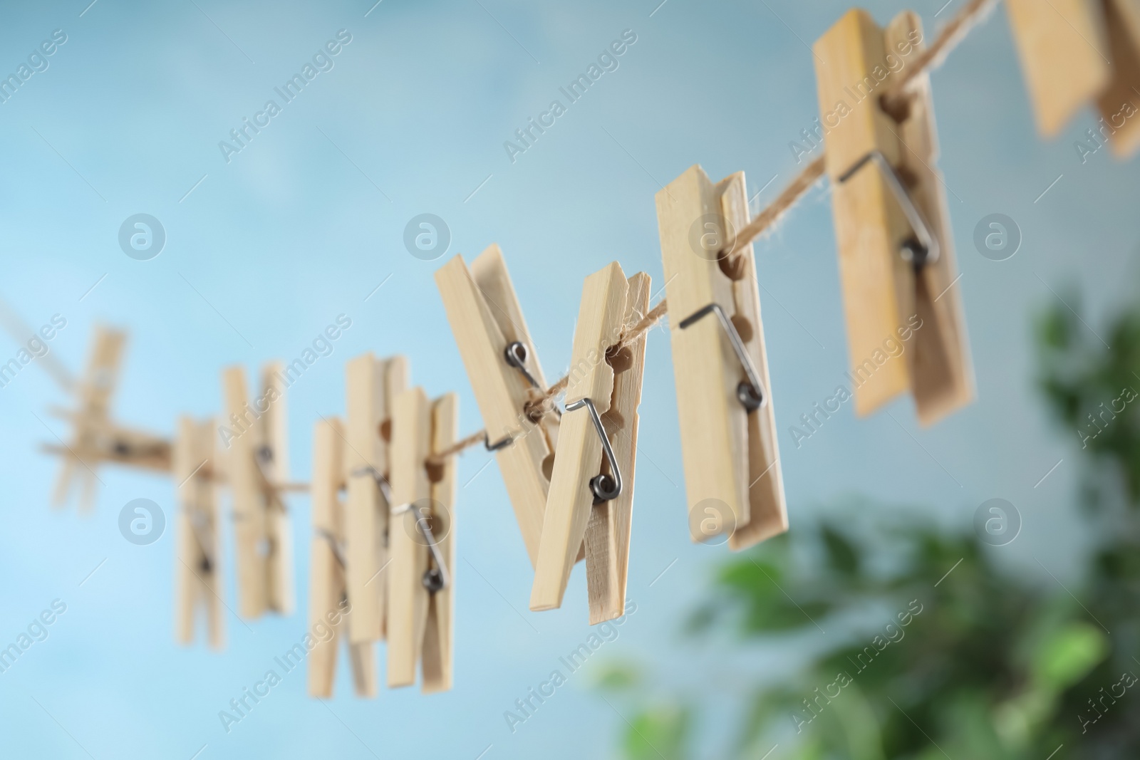 Photo of Wooden clothespins hanging on washing line against blurred background, closeup