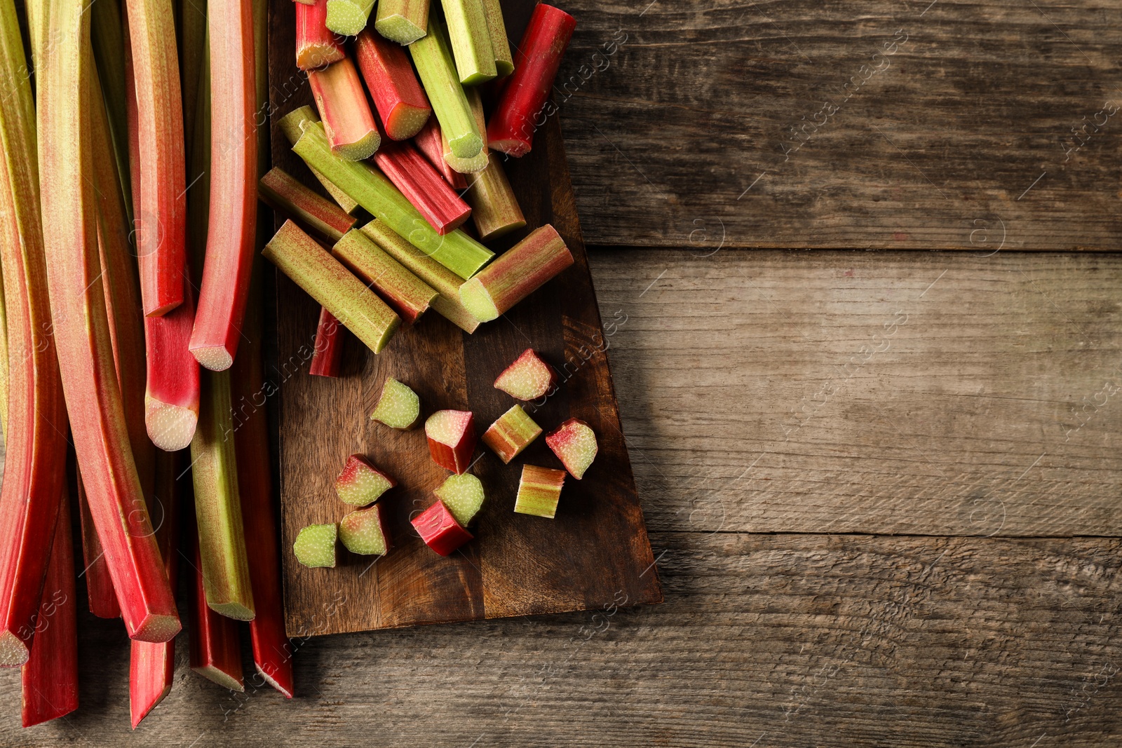 Photo of Many cut rhubarb stalks on wooden table, top view. Space for text