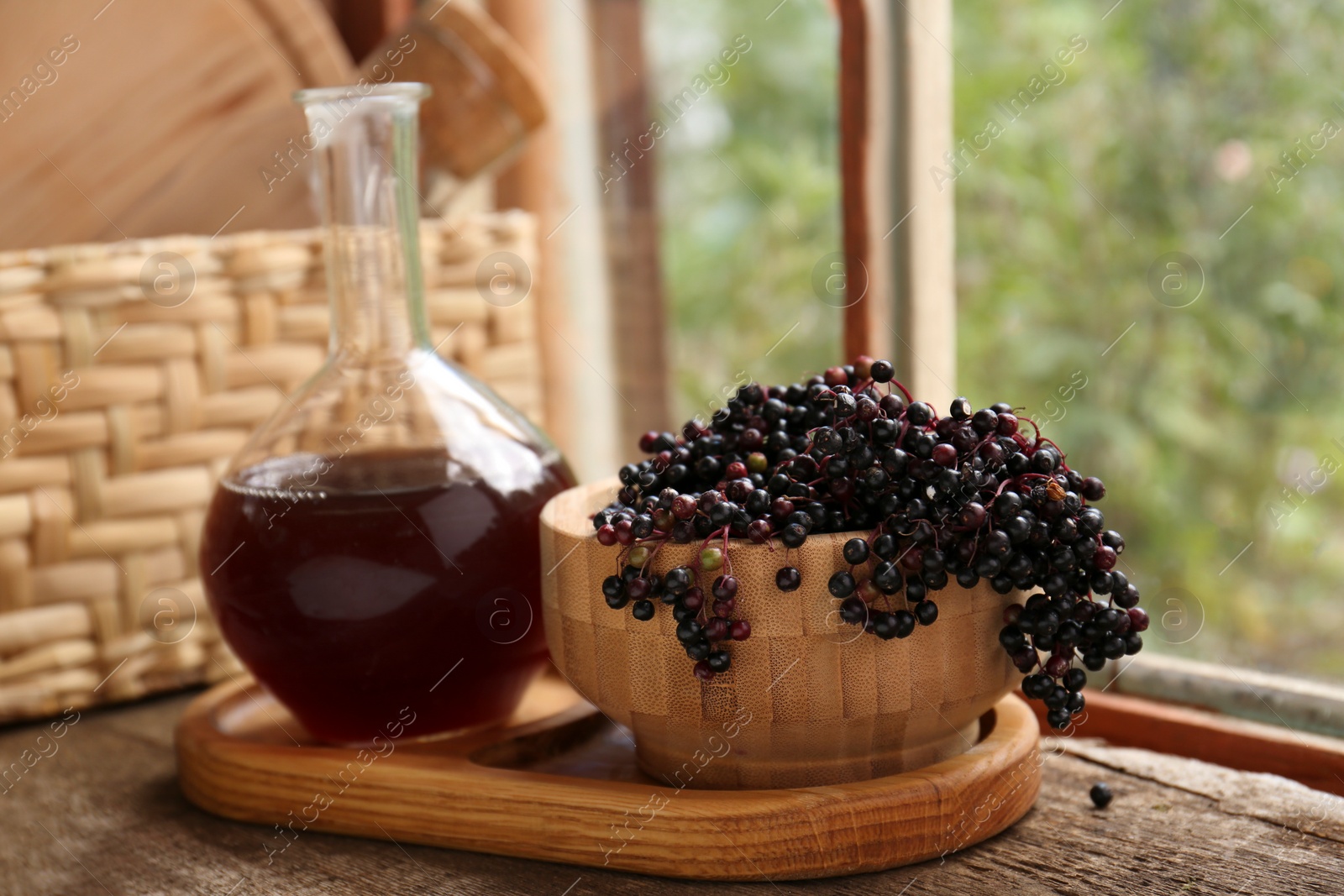 Photo of Elderberry wine and bowl with Sambucus berries on wooden table near window