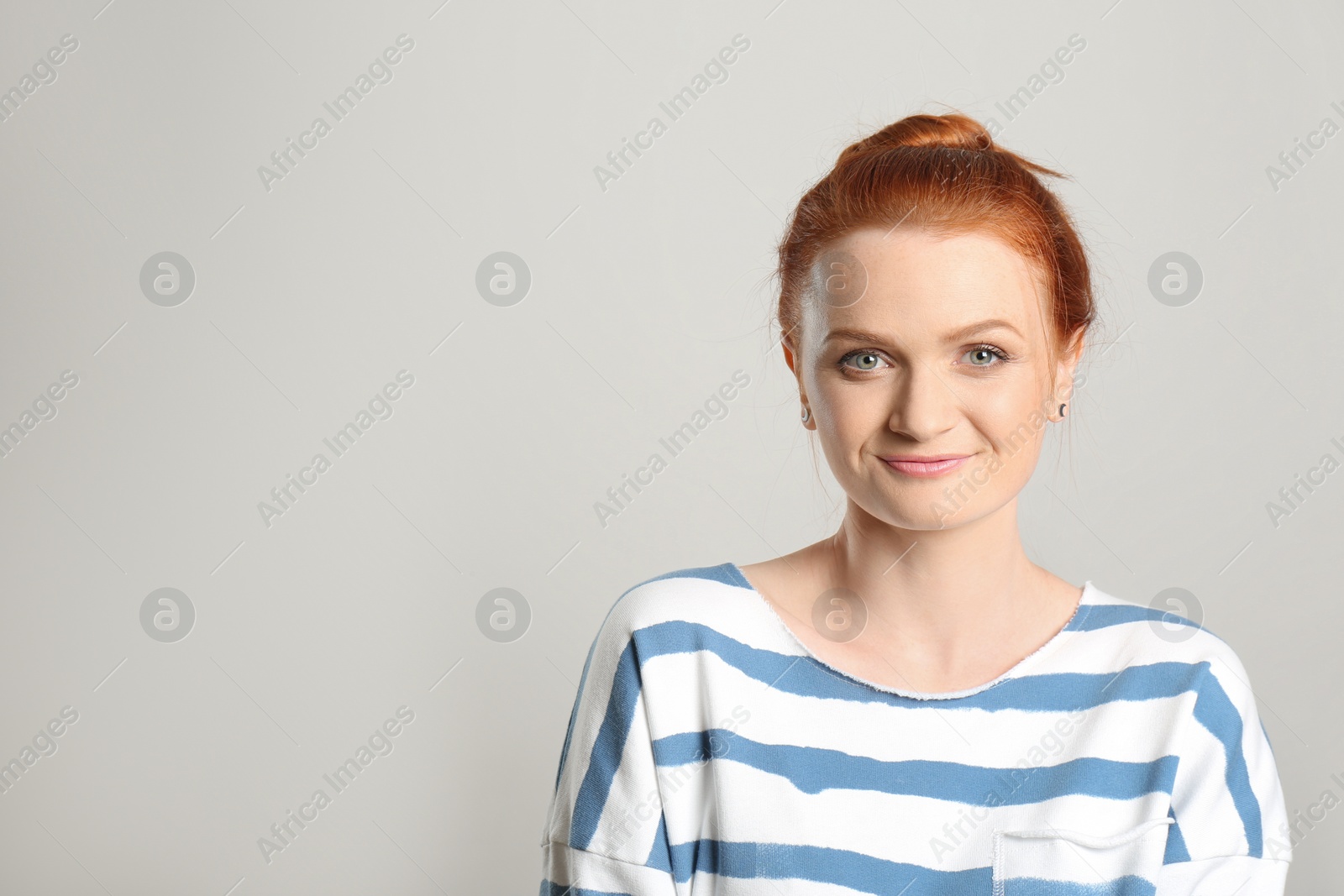 Photo of Candid portrait of happy red haired woman with charming smile on light background, space for text