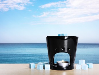 Image of Stylish aroma lamp with wax cubes on wooden table near sea, space for text