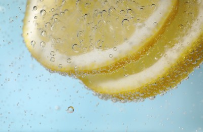 Photo of Juicy lemon slices in soda water against light blue background, closeup