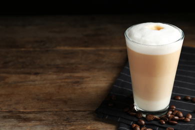 Photo of Delicious latte macchiato and coffee beans on wooden table. Space for text