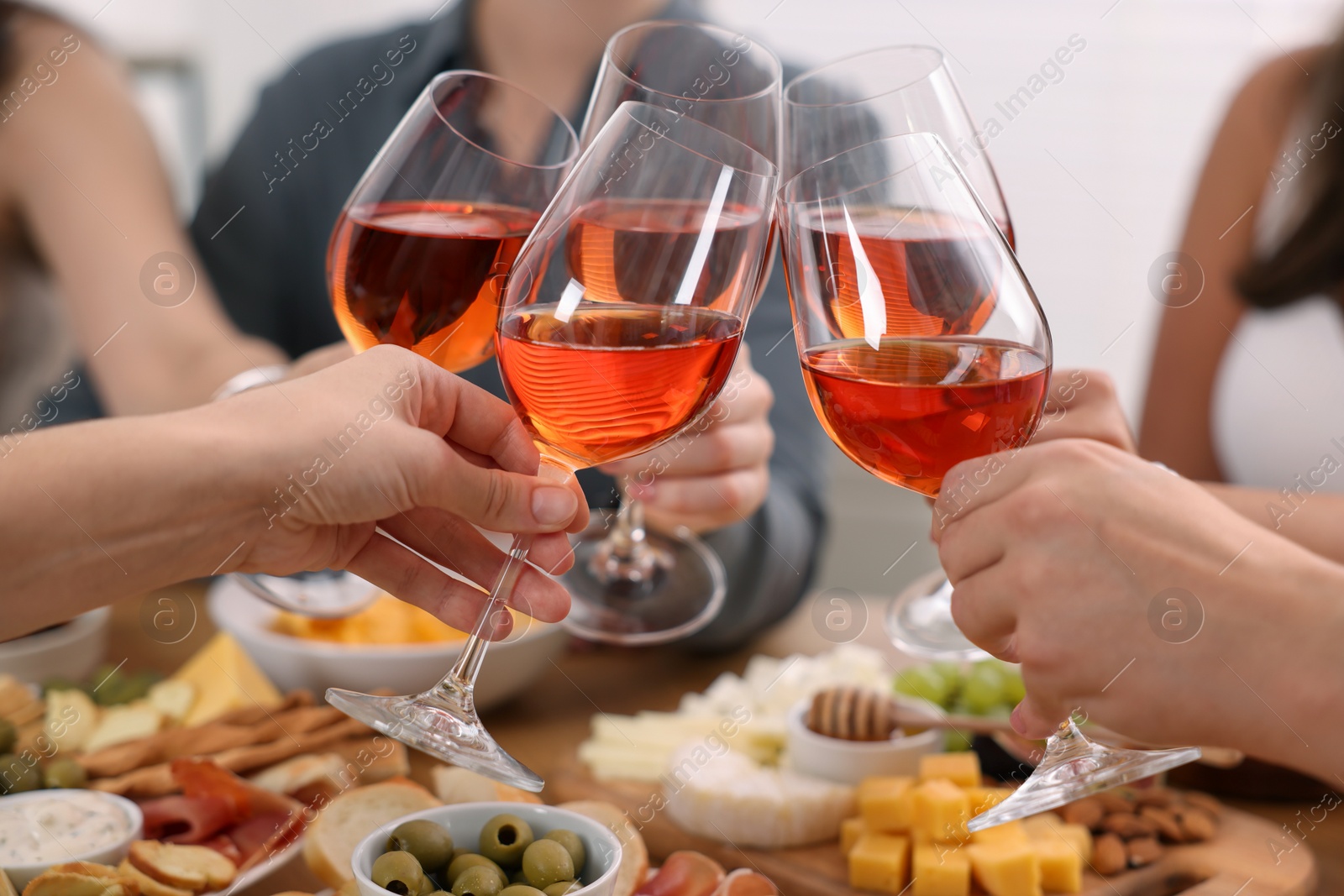 Photo of People clinking glasses with rose wine above wooden table indoors, closeup