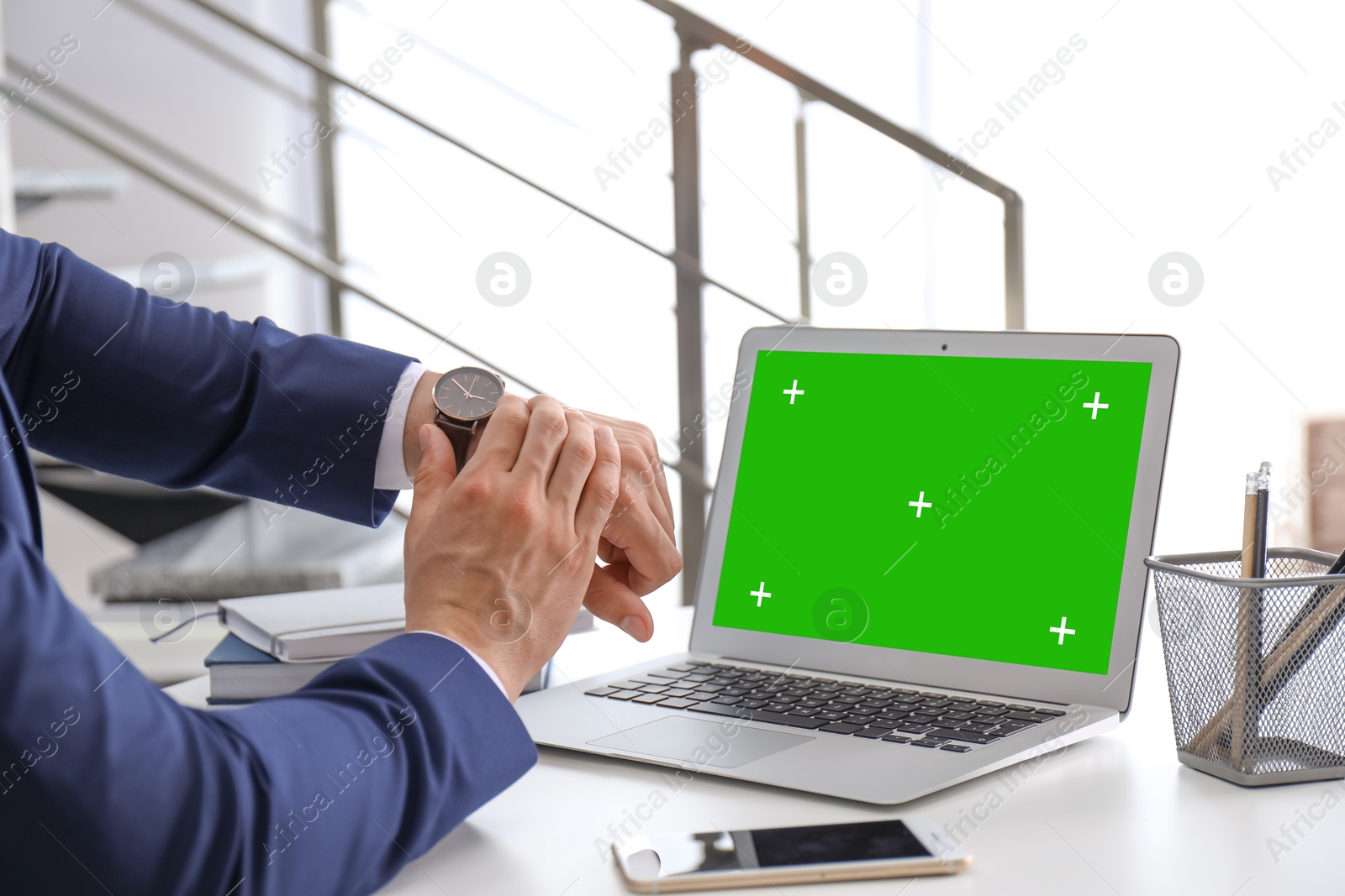 Image of Businessman checking time on his wristwatch at workplace. Laptop display with chroma key