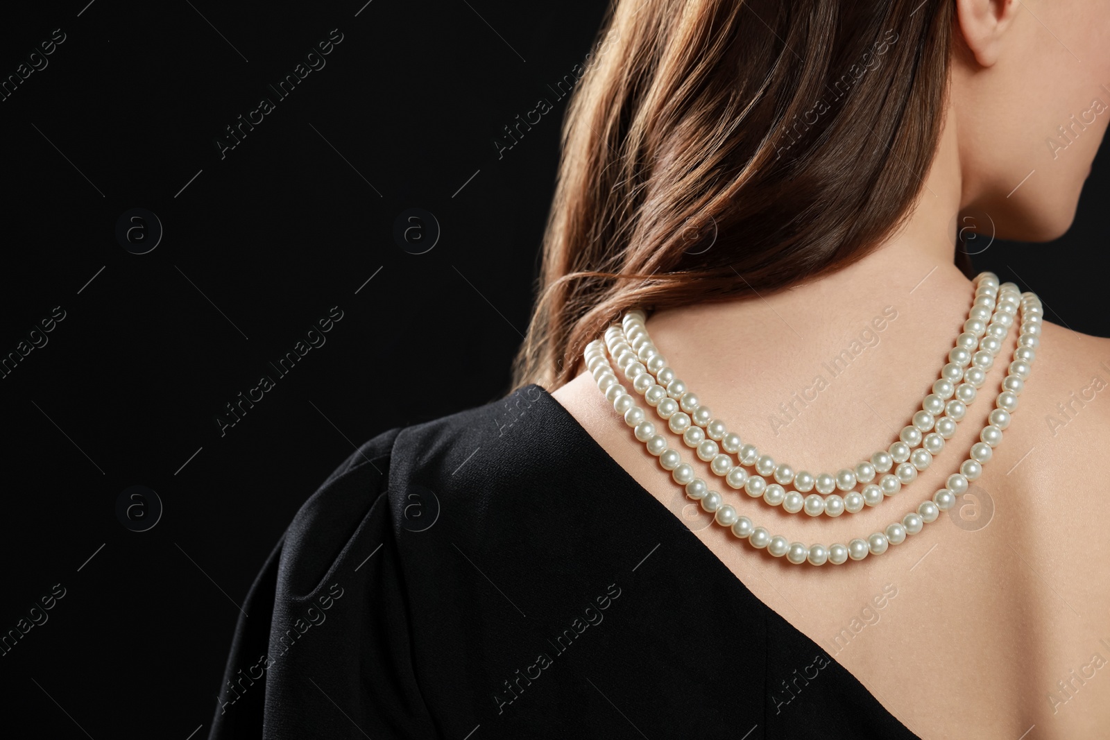 Photo of Young woman wearing elegant pearl necklace on black background, closeup. Space for text